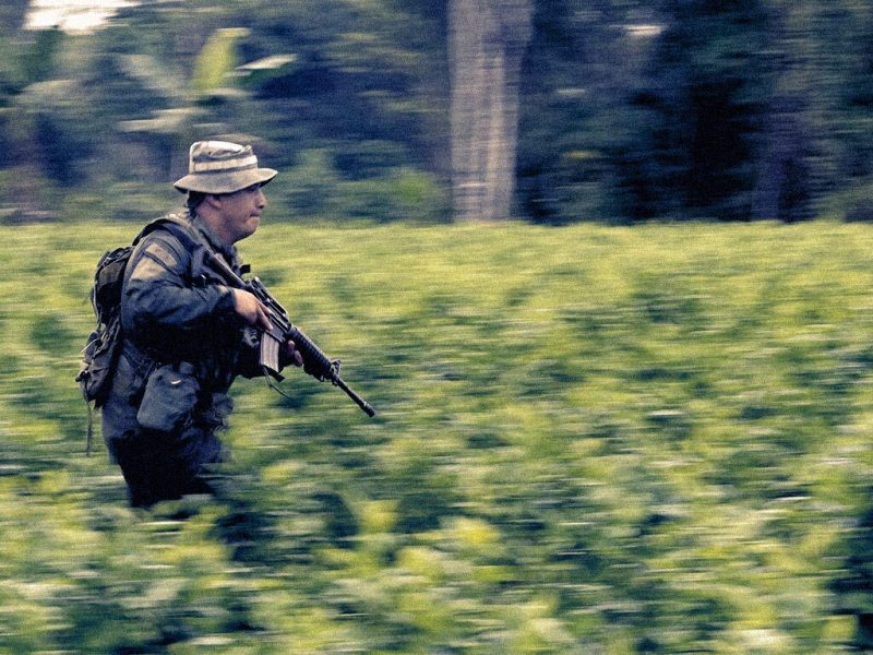 A soldier carrying a weapon running through a field of coca plants