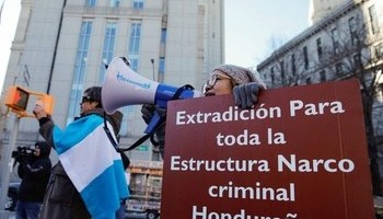 Protesters hold signs calling for extradition for all members of the "Honduran criminal narco structure." Manifestantes sostienen carteles que piden la extradición de todos los miembros de la "estructura narco criminal hondureña".