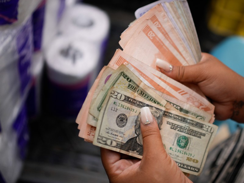 A vender counts Venezuelan Bolivars and US dollar bills to deliver change for a customer at a public market in the Quinta Crespo neighborhood in Caracas, Venezuela, Sunday, Dec. 11, 2022. Credit: