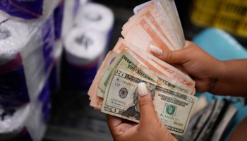 A vender counts Venezuelan Bolivars and US dollar bills to deliver change for a customer at a public market in the Quinta Crespo neighborhood in Caracas, Venezuela, Sunday, Dec. 11, 2022. Credit: 